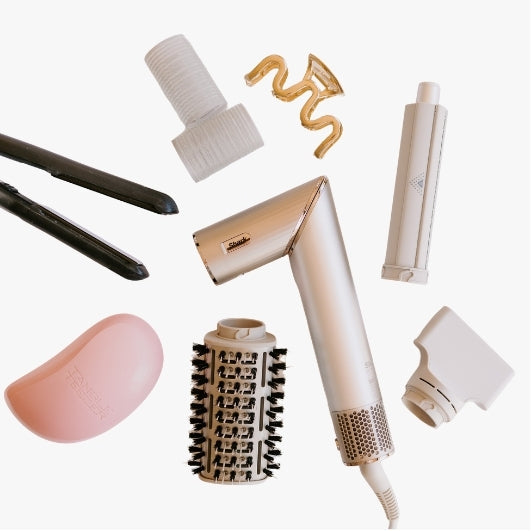 flat lay of hair tools for The Beauty Exchange, including brushes, hair clips. hair straighteners, rollers, hairdryer on a neutral background